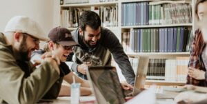 three men laughing while looking in the laptop inside room
