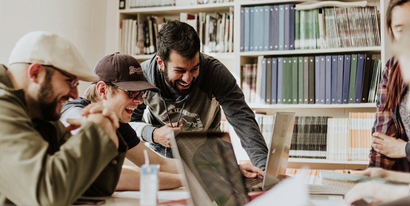 three men laughing while looking in the laptop inside room
